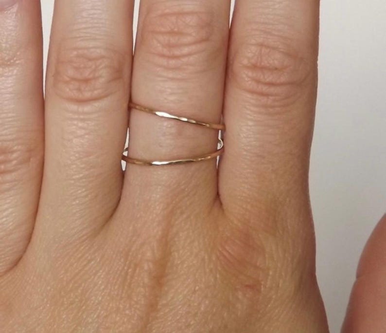 May include: Two thin gold rings on a finger. The rings are hammered and have a slightly irregular shape.