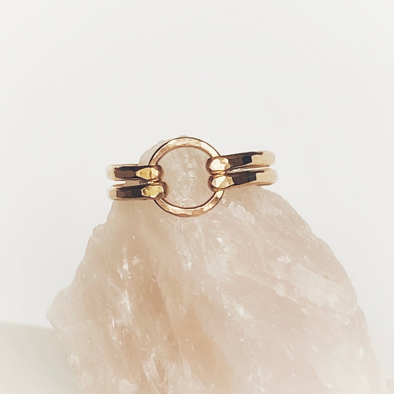 May include: A gold ring with a hammered finish and a circle design. The ring is made of two bands that are connected by a circle.
