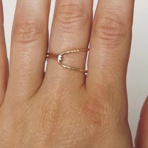 May include: A gold-toned ring with a simple, open design. The ring is made of two thin bands that cross over each other, creating a small, open space in the center.