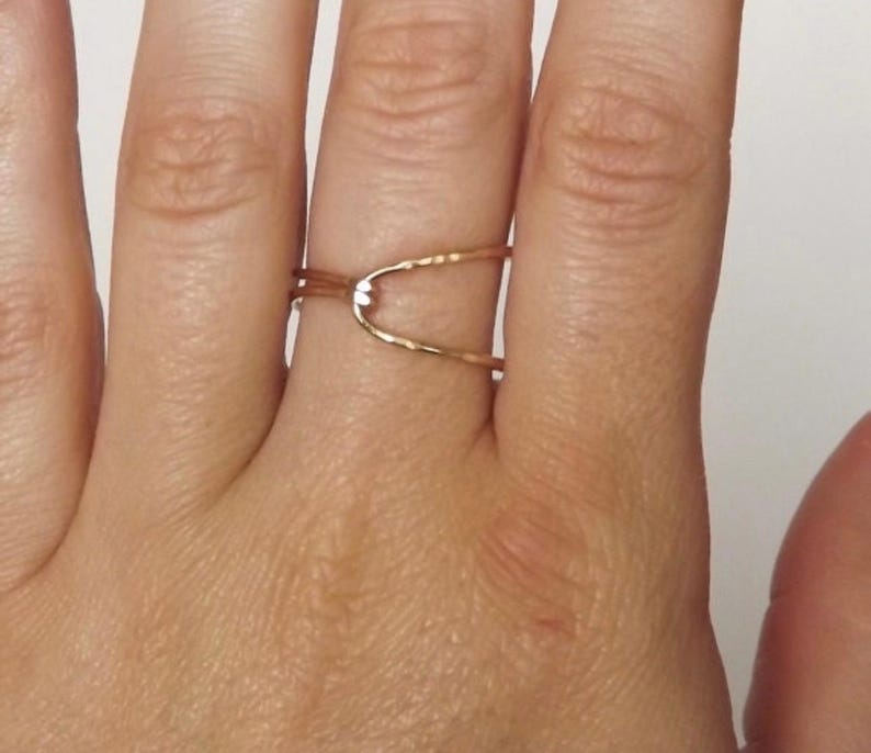 May include: A gold-toned ring with a simple, open design. The ring is made of two thin bands that cross over each other, creating a small, open space in the center.