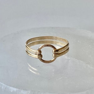 May include: A gold ring with a hammered finish and a circle design. The ring is made of two bands that are connected by the circle.