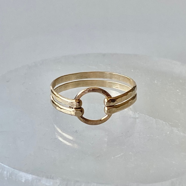 May include: A gold ring with a hammered finish and a circle design. The ring is made of two bands that are connected by the circle.