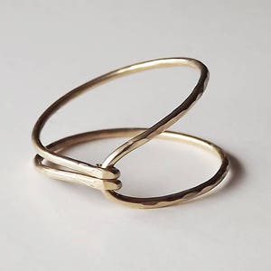 May include: A gold ring with a hammered finish and a unique open design. The ring is made of two bands that are connected at the top.