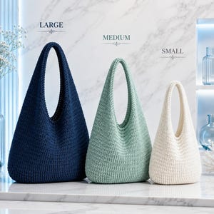 May include: Three hobo-style bags in a textured knit pattern, arranged by size and labelled as LARGE, MEDIUM, and SMALL. The largest bag is dark navy blue, the medium bag is sage green, and the smallest bag is off-white. Each bag features a single integrated handle.