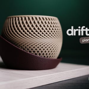 Puede incluir: Una maceta beige con un patrón tejido y un platillo burdeos oscuro. La maceta tiene forma esférica y se asienta sobre una superficie de color claro. La palabra "drift" se muestra en texto blanco, con "planter" en un rectángulo marrón.