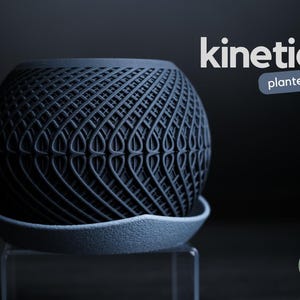 Op de afbeelding: Een donkerblauwe, bolvormige plantenbak met een uniek, geweven ontwerp, die op een bijpassende schotel staat. De plantenbak is gelabeld met "kinetic planter" in witte tekst. Het ontwerp heeft een herhalend patroon van gebogen lijnen.