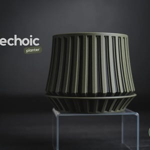 May include: An olive green Echoic planter with a vertical ribbed texture and a matching saucer base. The design features a wide top that tapers toward the bottom. The text echoic planter is visible in the upper left, and h3liø design is in the lower right.