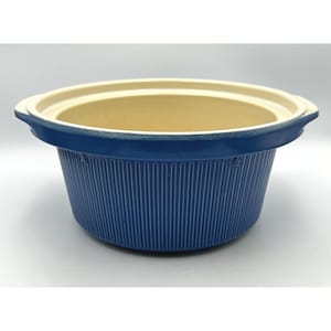 May include: A round ceramic baking dish with a vibrant blue exterior featuring a vertical ribbed texture and a smooth, cream-coloured interior. The vessel includes two integrated side handles and a wide, flat rim, providing a sturdy design.