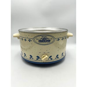 May include: A cream-coloured Rival Crock-Pot stoneware slow cooker with a blue speckled pattern and blue floral accents. The front features a control knob with settings for off, low, and high, and the text Rival Crock-Pot Stoneware Slow Cooker.
