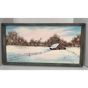 May include: A rectangular landscape painting in a dark gray wooden frame depicting a brown barn in a snow-covered field. A wooden fence runs across the foreground, leading toward the barn under a pale blue and pink sky with brown trees.