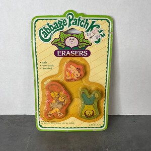 May include: A vintage Cabbage Patch Kids eraser set in original yellow blister packaging. The card features the brand logo, text stating safe, non-toxic, and scented, and three shaped erasers: a rabbit, a girl jumping rope, and a child doing a handstand.