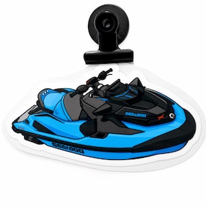 Puede incluir: Una pegatina troquelada con una ilustración de una moto de agua Sea-Doo en azul brillante y negro. El diseño incluye el logotipo de Sea-Doo en el lateral y en la parte delantera, con un clip negro sujeto al borde superior de la pegatina.