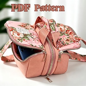 May include: A pink bag with a floral pattern featuring roses and green leaves, gold-toned metal zippers, and a top handle. The bag is partially open, revealing a blue smartphone inside. The text "PDF Pattern" is displayed at the top of the image.