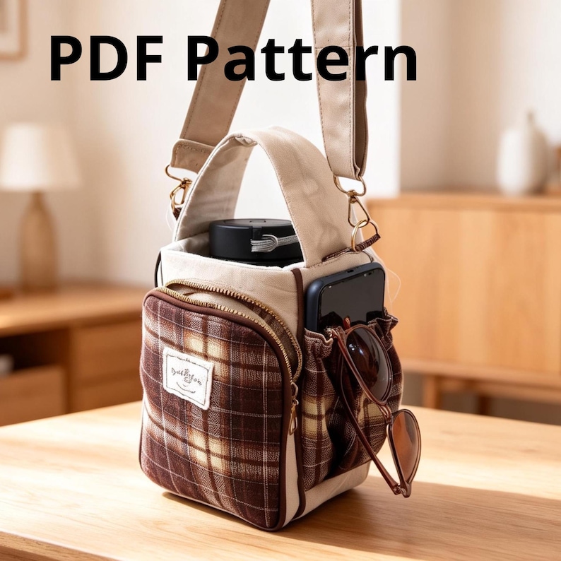 May include: A beige and brown plaid crossbody bag with a top handle and adjustable strap. The bag features a front zippered pocket with a white label, a side pocket holding a smartphone and sunglasses, and a main compartment containing a black bottle. The text PDF Pattern is visible at the top.
