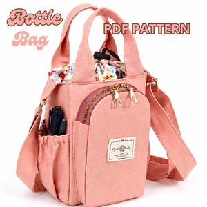 May include: A peach-colored bottle bag with two top handles and an adjustable shoulder strap. It features a front zippered pocket, a side pocket containing two pens, and a drawstring closure with a floral interior lining. Text reads Bottle Bag PDF PATTERN.