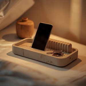 May include: A rectangular light-coloured stone valet tray with a smooth finish and subtle veining. The tray features a built-in vertical stand for a smartphone and a grooved section for organising small items like a set of metal keys.