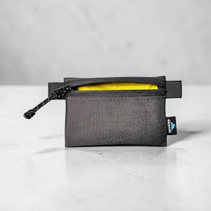 May include: A small rectangular black zippered pouch with a textured fabric exterior. The pouch features a bright yellow interior lining, a black zipper pull with a cord, and a small black tag on the side with the text WESTON in white.