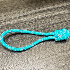May include: A turquoise rope loop with a gray accent, knotted at one end. The rope is lying on a wooden surface. The loop is a bright, eye-catching color.