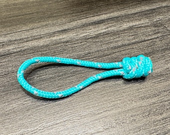 May include: A bright turquoise zipper pull made of braided cord with reflective silver flecks woven throughout. The cord is looped and secured with a tight, decorative knot at one end, creating a functional handle for easy gripping.