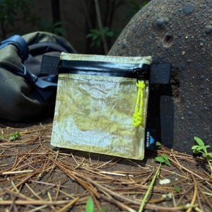 May include: A small, translucent yellow pouch with a black zip and a neon yellow pull cord. The pouch has black fabric loops on each side. The brand name "WESTON" is printed on a small black tag.