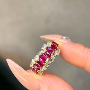 Peut inclure: Une bague en or ornée d'une rangée de rubis rouges vifs de forme ovale, entrecoupés de plus petites pierres précieuses transparentes. Le design de la bague présente un sertissage délicat et orné, créant un bijou luxueux et attrayant.