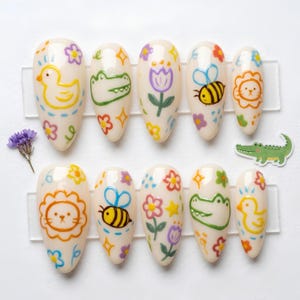 May include: A set of ten almond-shaped press-on nails with a cream base, featuring hand-painted colorful doodles of yellow ducks, green crocodiles, purple tulips, striped bees, and orange lions, accented with small stars and flowers.