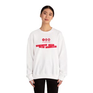 Pode incluir: Camisola branca com texto e gráficos vermelhos. O texto inclui "BTS WORLD TOUR" e os nomes "J-HOPE" e "JUNG-KOOK". A camisola tem gola redonda e mangas compridas. O design apresenta uma série de barras horizontais vermelhas.