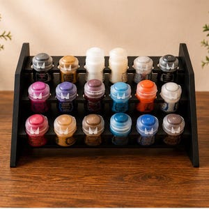 Peut inclure: Un présentoir à étages en bois noir contenant dix-huit petits pots de peinture avec des couvercles translucides. Les pots sont disposés en trois rangées de six, présentant une variété de couleurs dont le blanc, le bleu, le violet, l'orange, l'or et le gris.