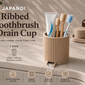 May include: A beige cylindrical toothbrush drain cup with a vertical ribbed texture. The cup holds a tube of toothpaste and three toothbrushes. It features a small spout at the base for water drainage. Text on the image reads: Japandi Ribbed Toothbrush Drain Cup, Minimal Form. Calm Function. 1 Size, 80 x 105 mm.
