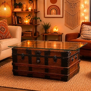 May include: A rectangular coffee table featuring a vintage wooden trunk base with dark metal hardware and a clear glass top. The trunk has horizontal wooden slats, reinforced corners, and a central latch mechanism, providing a sturdy surface.