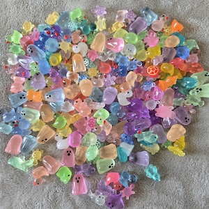 May include: A large collection of small, translucent, multi-colored plastic figurines in various shapes, including ghosts, turtles, ducks, and other creatures. Each piece features a smooth, glossy finish and simple painted facial details.