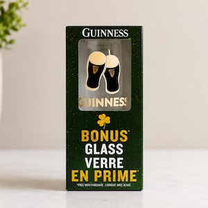 May include: A dark green box with the Guinness logo and a clear window displaying a pint glass. The box also features the words "BONUS GLASS VERRE EN PRIME" in yellow.