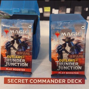 May include: Two Magic: The Gathering card packs and a blue card storage box. The packs are labelled "Outlaws of Thunder Junction" and "Play Booster." The text "Secret Commander Deck" is on a red label.