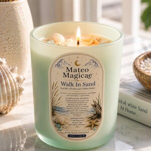 Könnte beinhalten: Eine mattierte hellgrüne Glaskerze mit brennendem Docht, verziert mit kleinen Muscheln und einem Seestern. Das Etikett zeigt Mateo Magicae Walk In Sand, Sea Salt, Driftwood, White Amber und 8 oz | 226 g. Die Kerze hat ein Küstenmotiv.