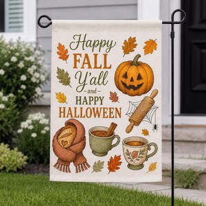 May include: A rectangular garden flag featuring the text Happy FALL Y'ALL and HAPPY HALLOWEEN. The design includes a carved orange jack-o'-lantern, a wooden rolling pin on a spider web, two mugs of warm drinks, and a loaf of bread wrapped in a scarf.
