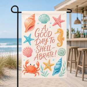 May include: A rectangular garden flag featuring a cream background with various colorful sea creatures including a crab, seahorse, starfish, and seashells. The text in the center reads A GOOD DAY TO SHELL-ABRATE! in a red cursive font.