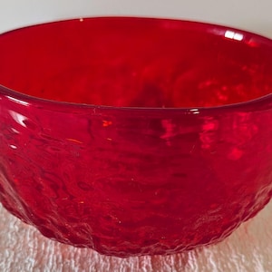 Könnte beinhalten: Eine leuchtend rote Glasschale mit strukturierter Außenseite. Die Schale hat ein breites, offenes Design und einen glatten, glänzenden Innenraum. Die strukturierte Oberfläche verleiht diesem dekorativen Stück visuelles Interesse.
