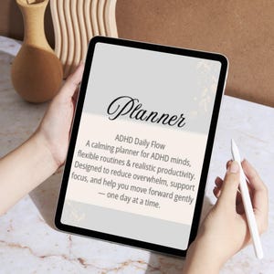 Op de afbeelding: Een tablet toont een digitale planner, vastgehouden door handen. Het scherm toont het woord "Planner" in sierlijke letters, met tekst eronder die het beschrijft als een ADHD dagelijkse flow planner om overbelasting te verminderen en focus te ondersteunen.