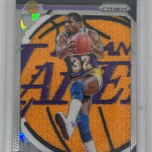 May include: A Magic Johnson basketball card featuring a player in a Lakers uniform, holding a basketball. The card has a purple and gold Lakers logo and the text "MAGIC JOHNSON". The card is encased in a clear protective holder.