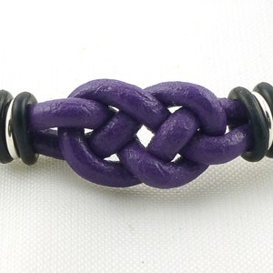 Puede incluir: Un brazalete de cuero morado con un dise&ntilde;o de nudo y detalles en negro y plata.