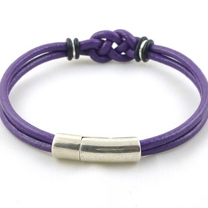 Puede incluir: Un brazalete de cuero morado con un cierre magn&eacute;tico plateado y un dise&ntilde;o de nudo trenzado.