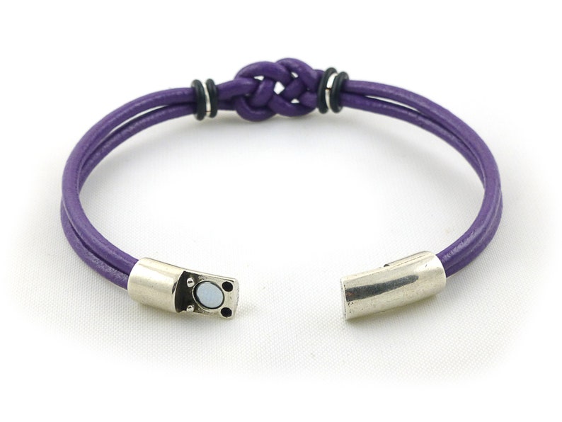 Puede incluir: Un brazalete de cuero morado con un cierre magn&eacute;tico plateado y un dise&ntilde;o de nudo trenzado.