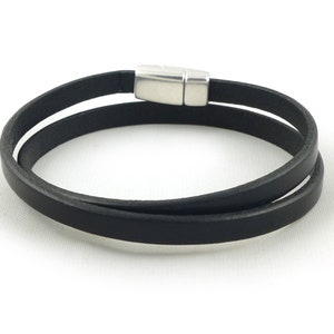 May include: A black leather bracelet with a silver magnetic clasp. The bracelet is double-layered and has a simple design.
