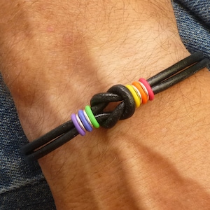 May include: A black leather bracelet with a knotted design and rainbow colored rings.