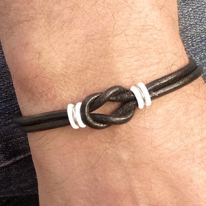 May include: A black leather bracelet with a knotted design and silver accents.
