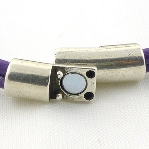 Puede incluir: Un brazalete de cuero morado con un cierre magn&eacute;tico plateado. El cierre tiene una peque&ntilde;a piedra redonda blanca en el centro.