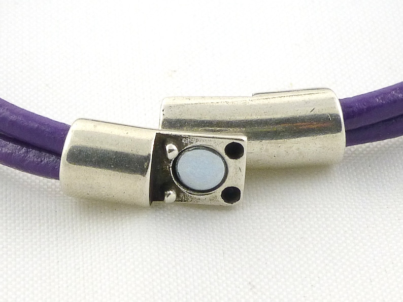 Puede incluir: Un brazalete de cuero morado con un cierre magn&eacute;tico plateado. El cierre tiene una peque&ntilde;a piedra redonda blanca en el centro.