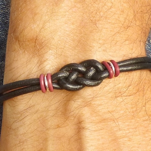 May include: A black leather bracelet with a knotted design and two burgundy rings.