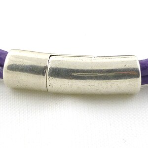 Puede incluir: Un brazalete de cuero morado con un cierre magn&eacute;tico plateado.