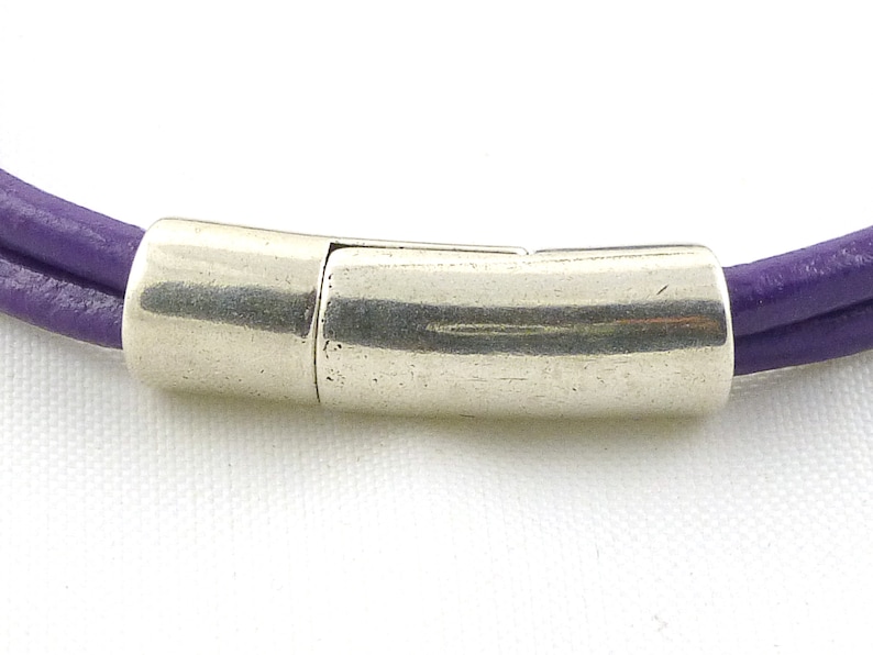 Puede incluir: Un brazalete de cuero morado con un cierre magn&eacute;tico plateado.